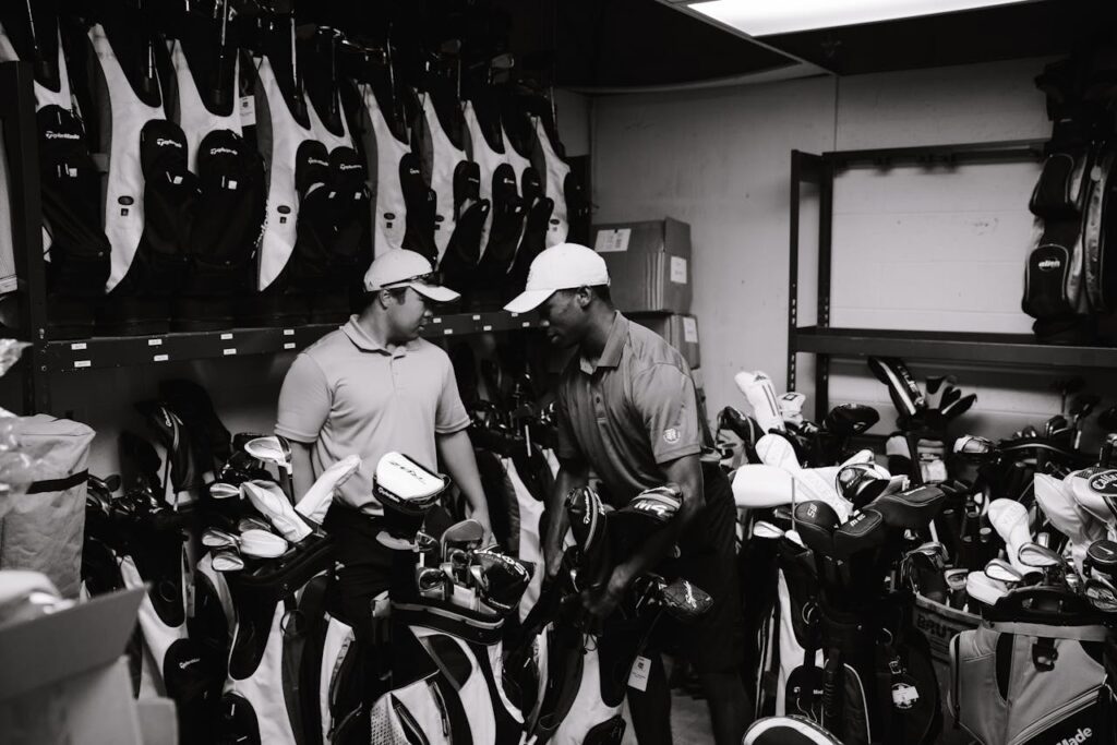 Two men sorting and organizing golf bags and clubs in a storage room.